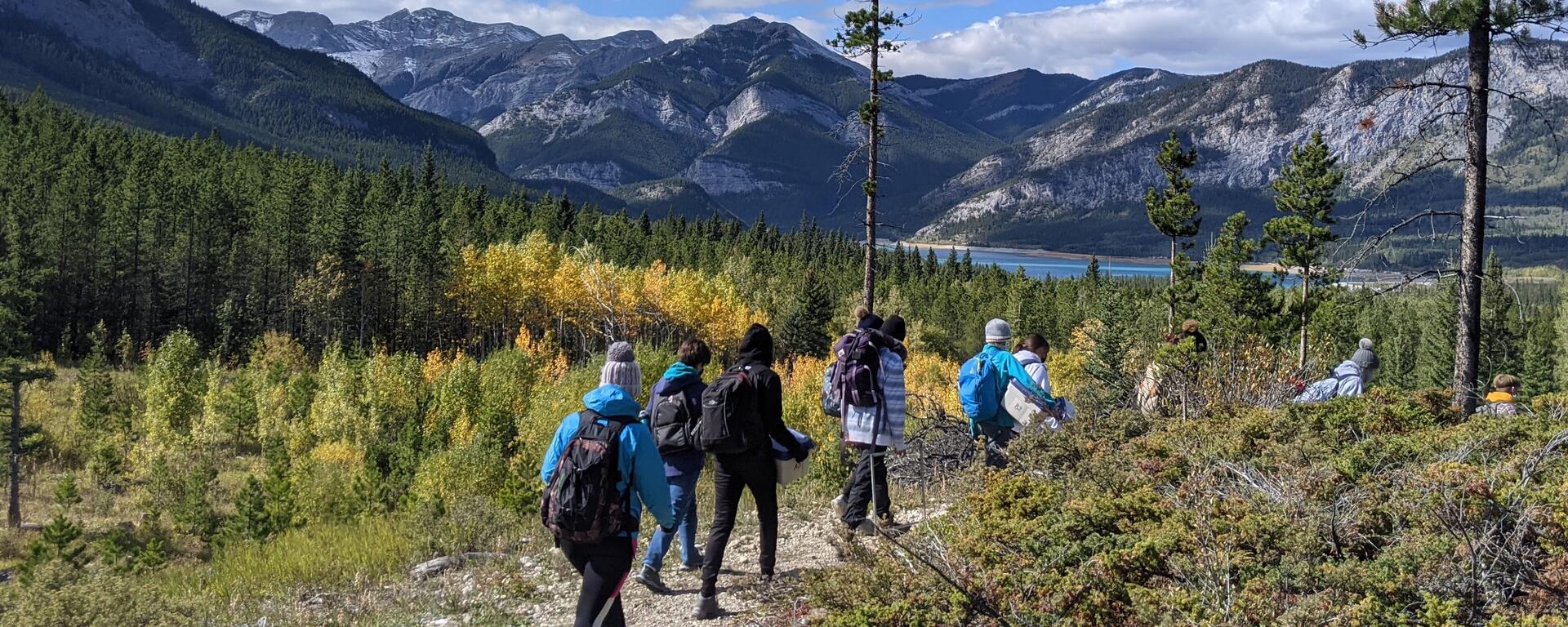 People walking a trail with a lake and mountains in the background. 