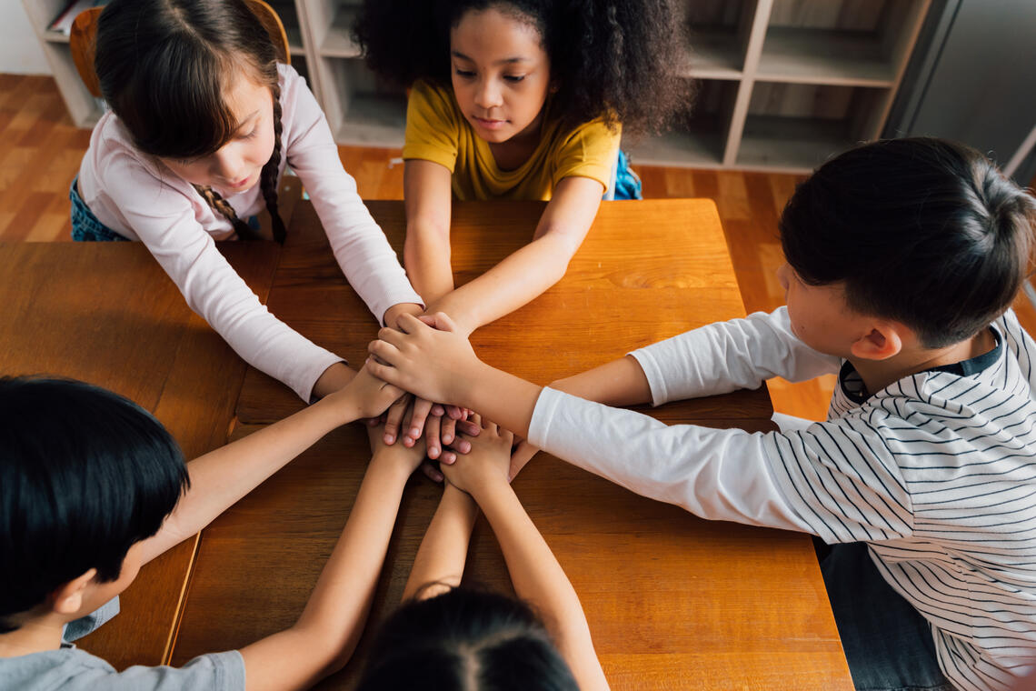 kids sitting at table holding hands
