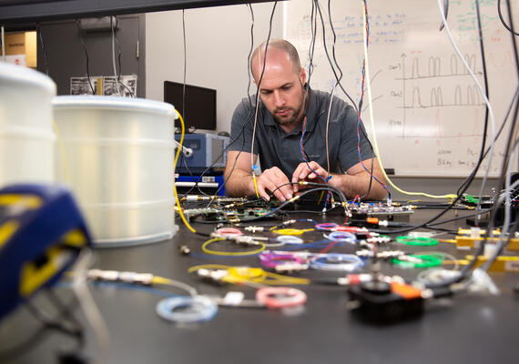 Man assembling two piece of wire at a lab bench, surrounded by computer parts. 