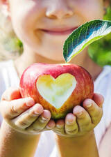 young girl holding an apple with a heart bite taken out of it